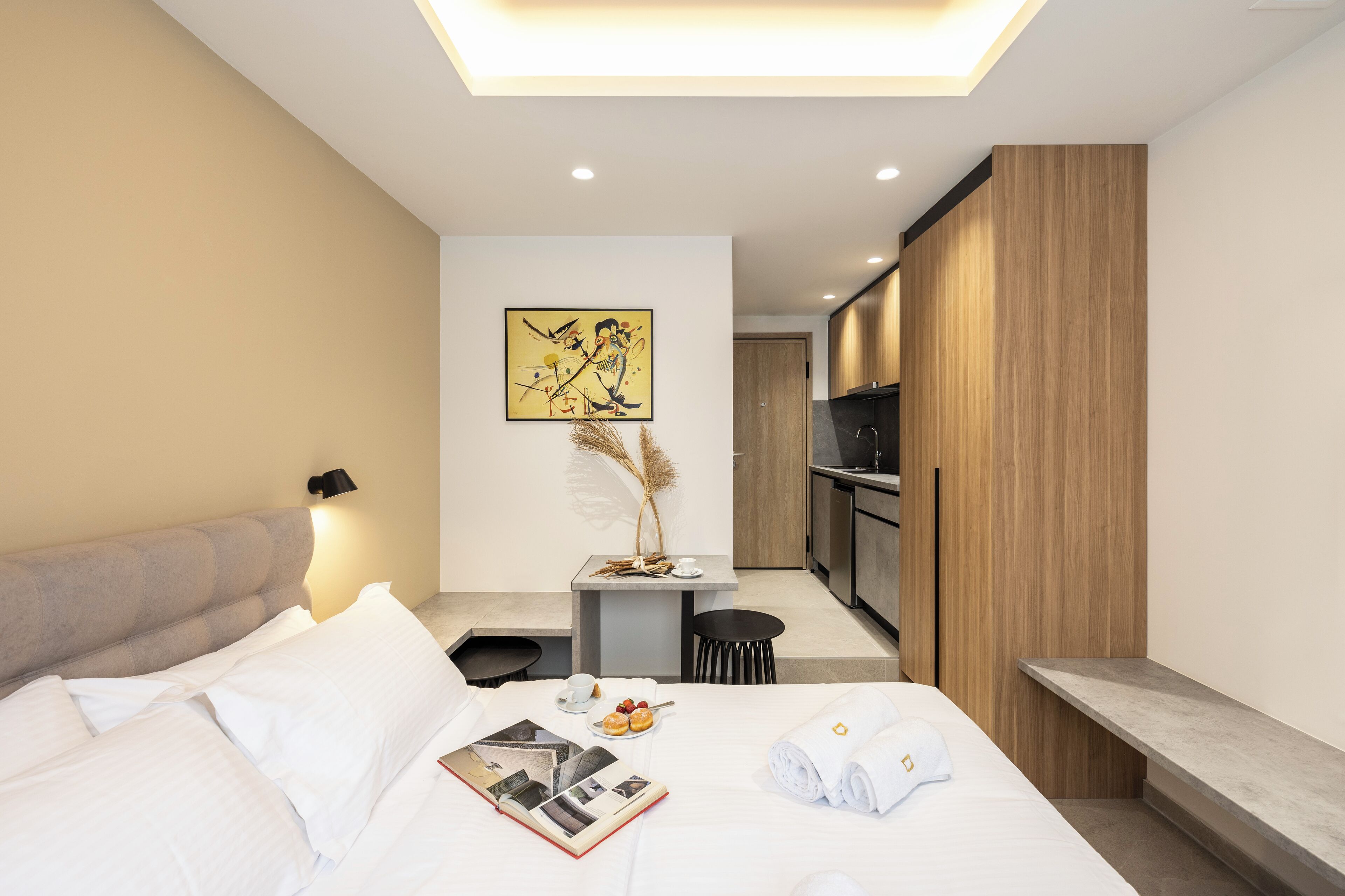 Una habitación de hotel moderna con una cama, mesita de noche y una pequeña zona de kitchenette.