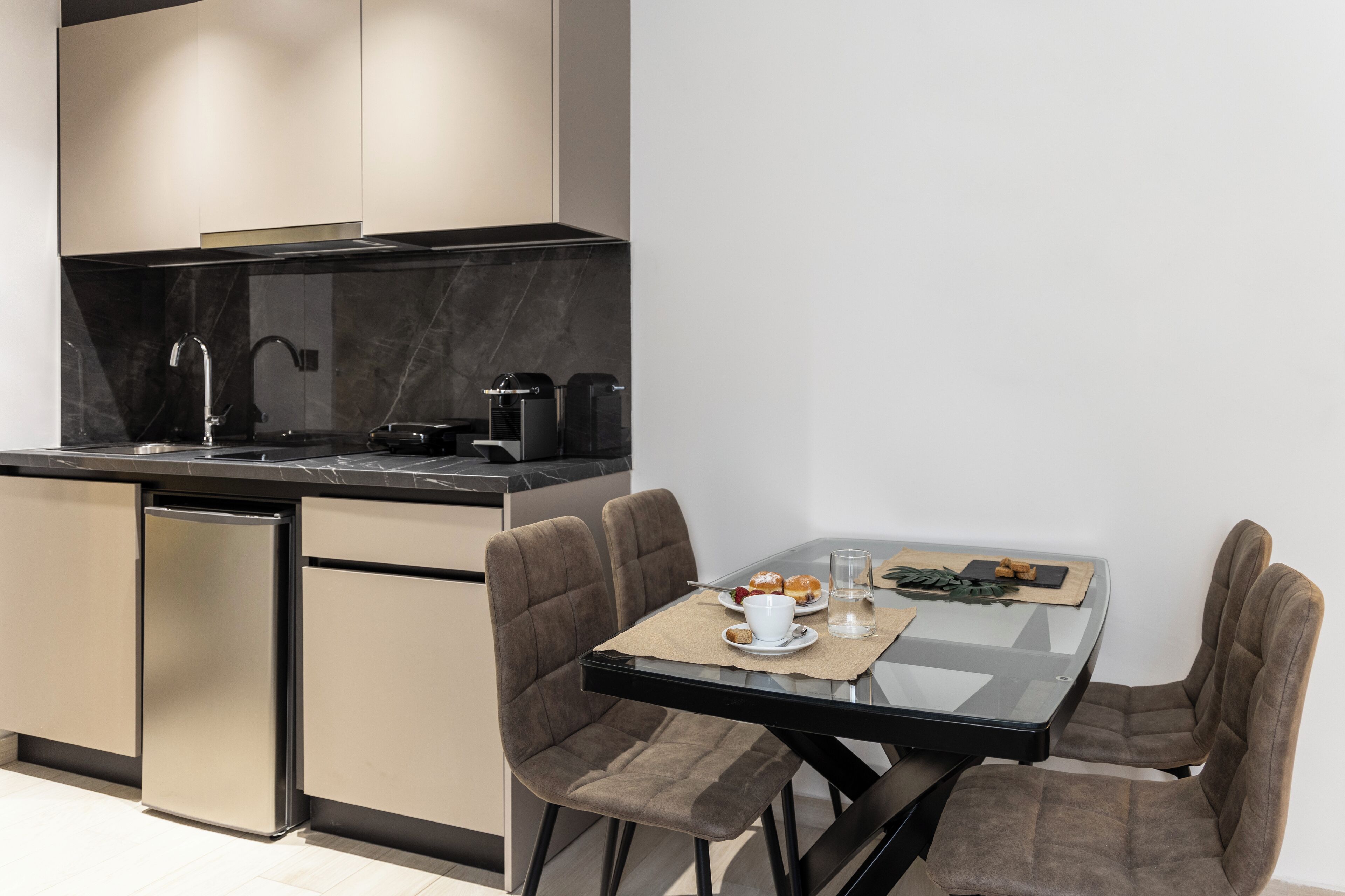 A modern kitchen with a built-in dishwasher, a coffee machine, and a dining area with a glass table and four chairs.