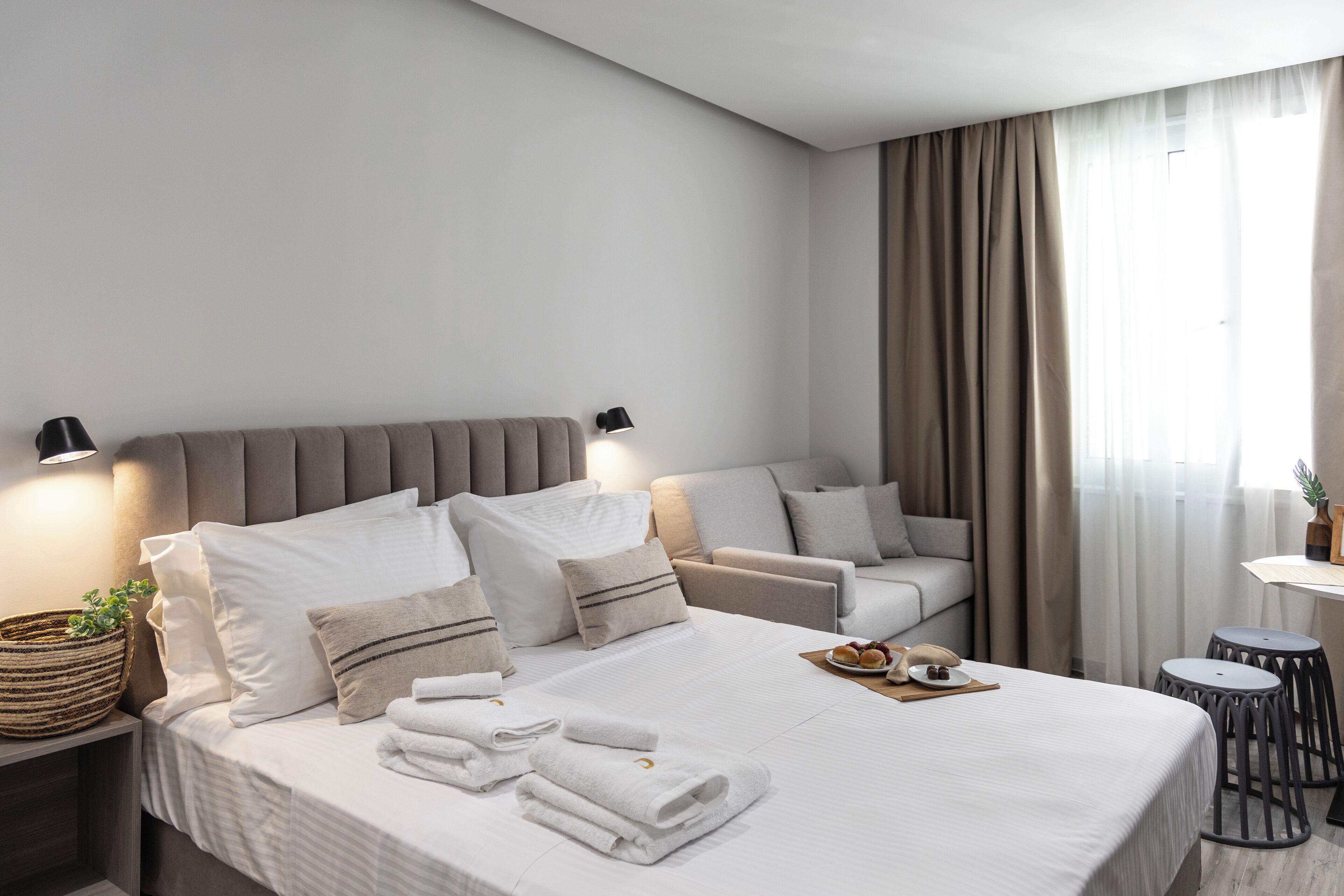Ett modernt hotellrum med en stor säng, två sängbord, en soffa och ett litet bord med en växt.