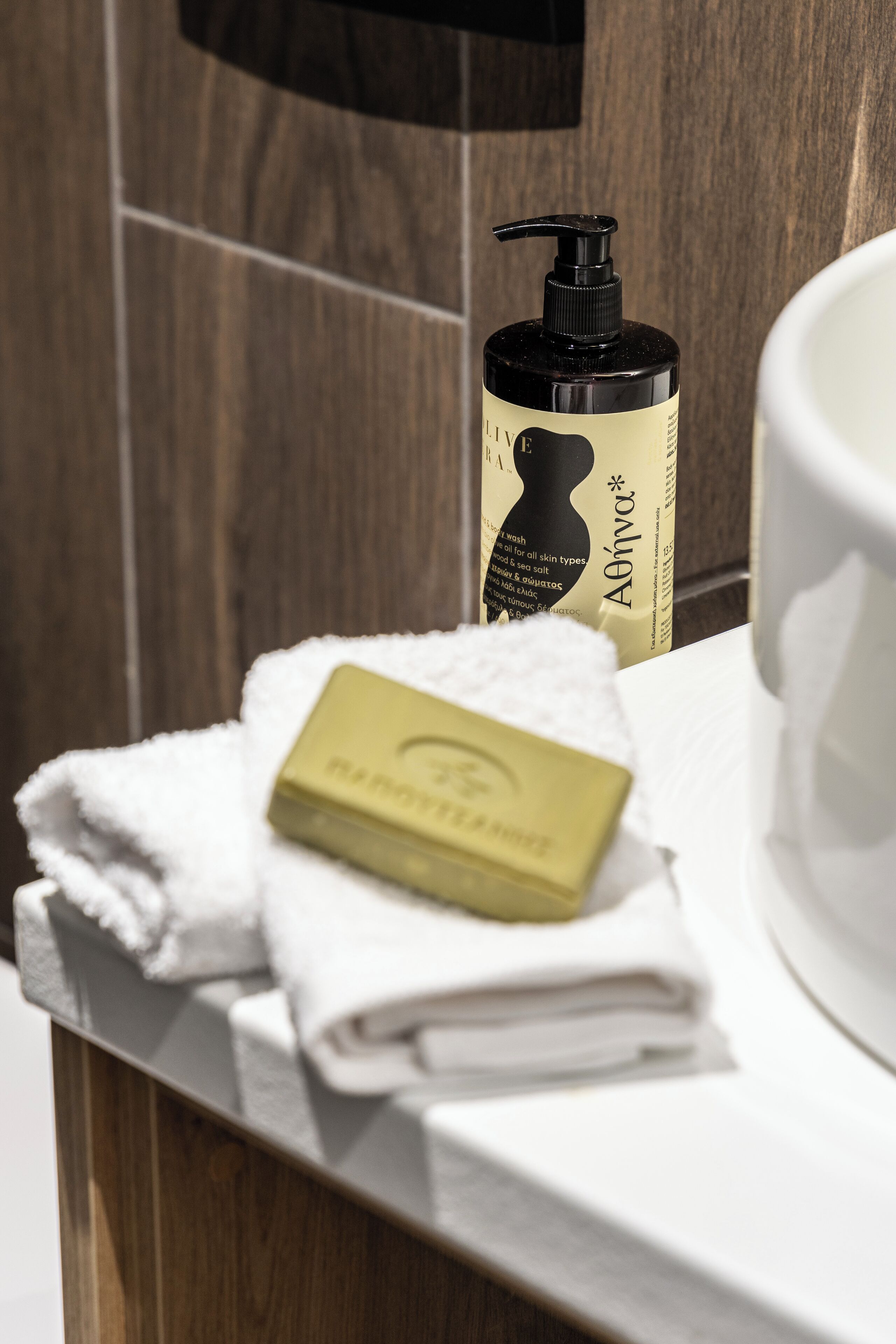 A bathroom with a wooden wall, a white sink, a bottle of soap, and a folded towel.