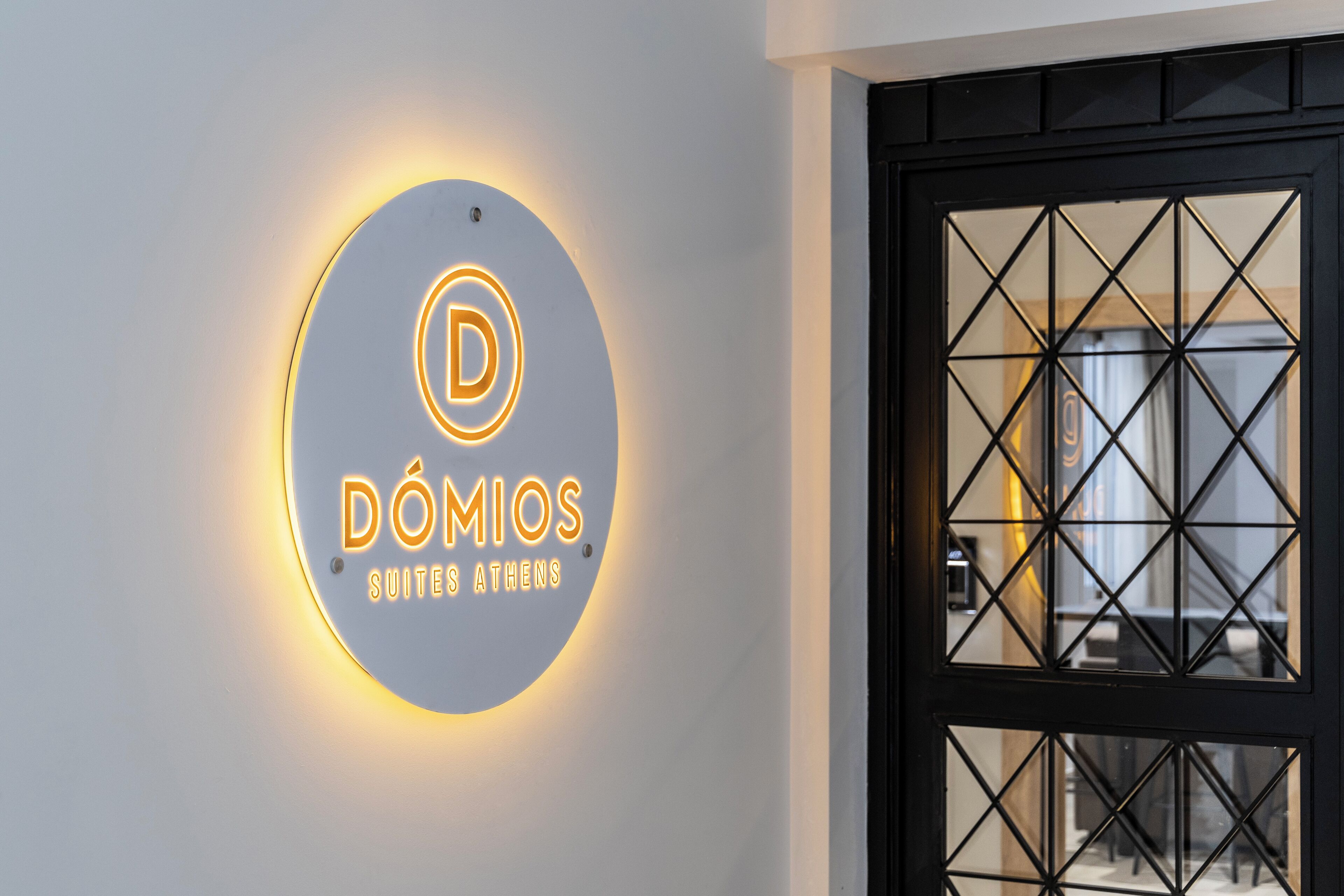 A circular illuminated sign with the text "DOMIOS SUITES ATHENS" on a wall.