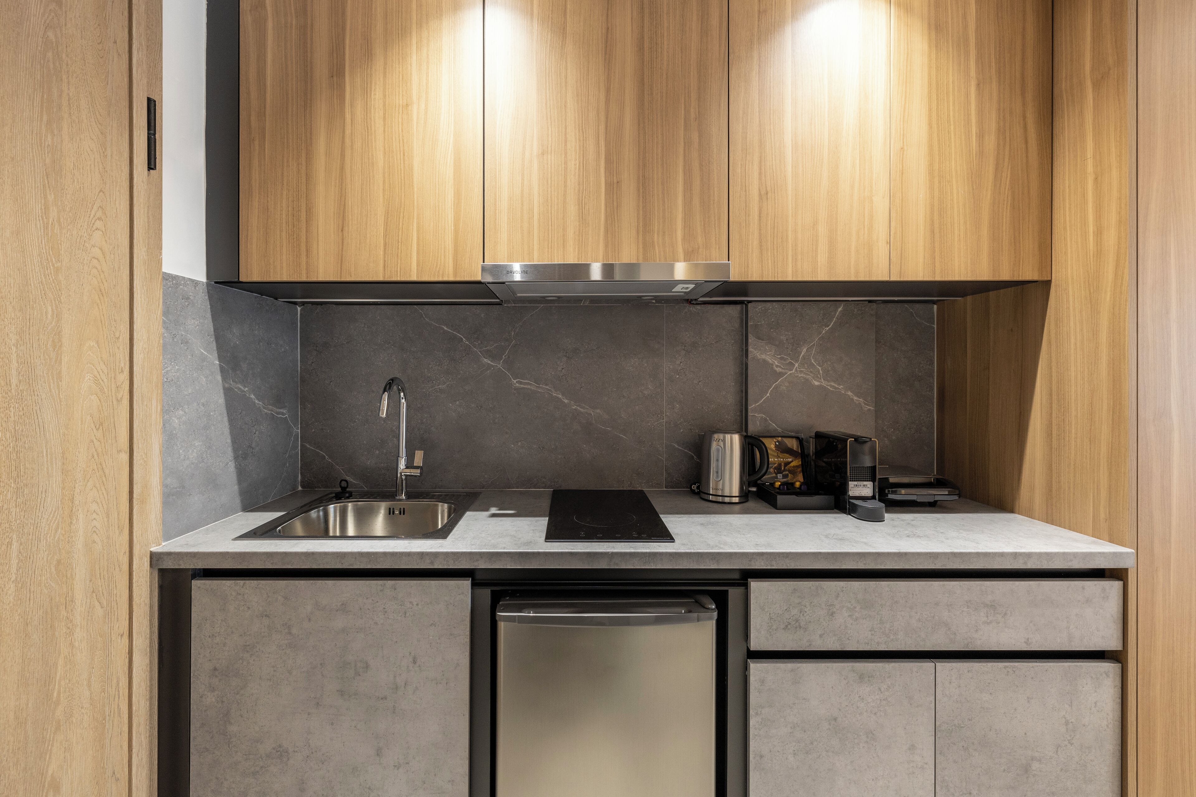 A modern kitchen with wooden cabinets, a stainless steel sink, a built-in dishwasher, and a marble backsplash.