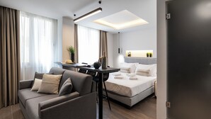 A modern hotel room with a sofa, a small table, a bed, and a desk. - DOMIOS Suites Athens (Athens)