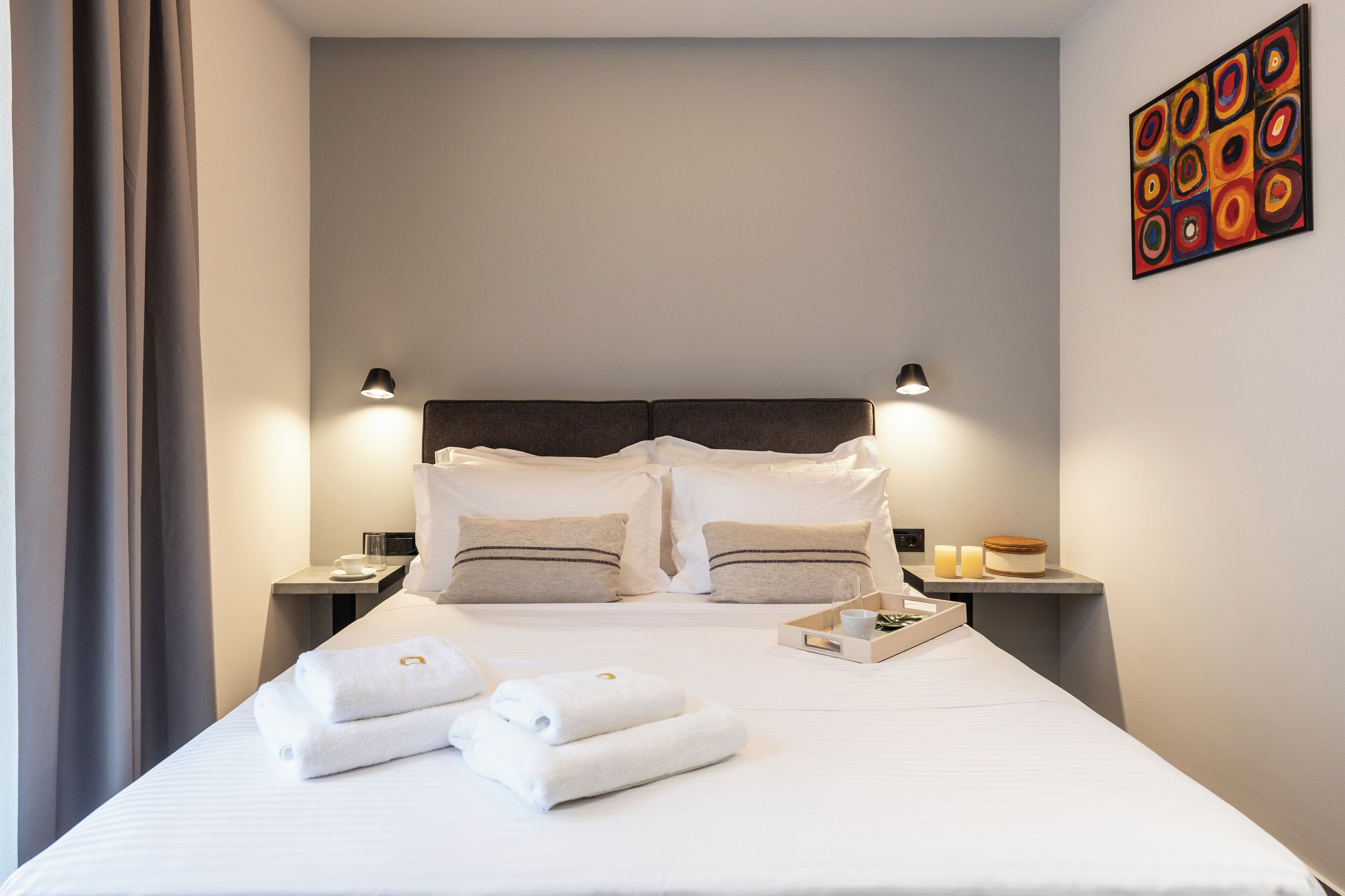 A neatly made bed with white linens and towels, a headboard, bedside tables with lamps, and a wall art piece.