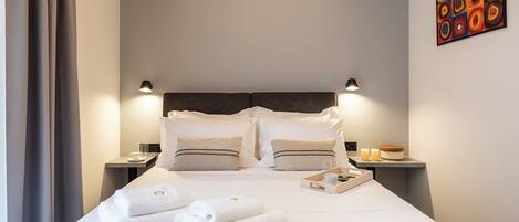 A neatly made bed with white linens and towels, a headboard, bedside tables with lamps, and a wall art piece.