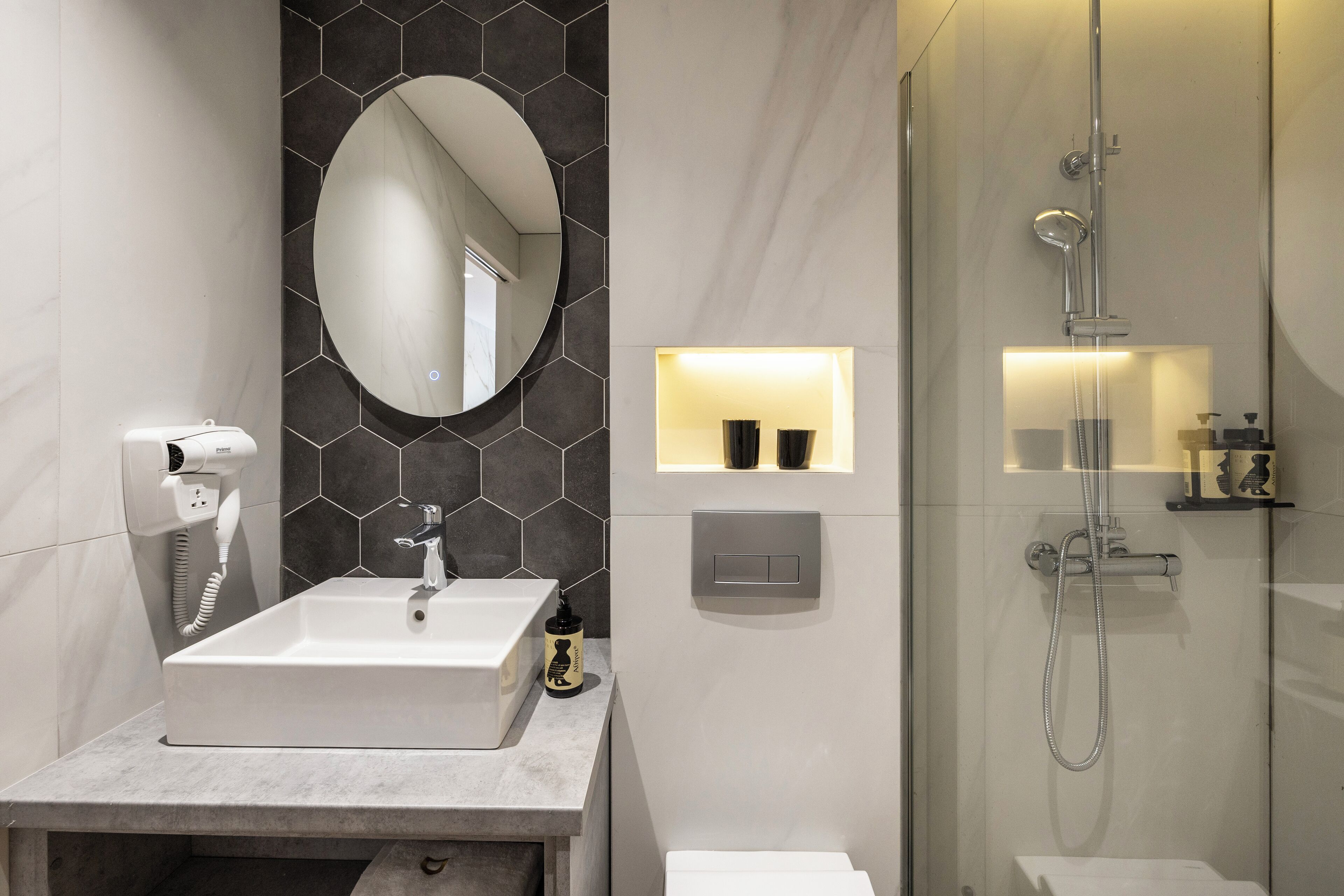 A modern bathroom with a large mirror, a sink, a shower, and a hairdryer.