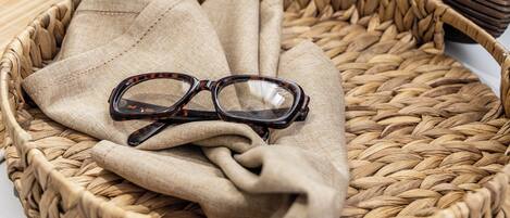 A woven basket with glasses and a fabric on a table, a framed picture, and two potted plants.
