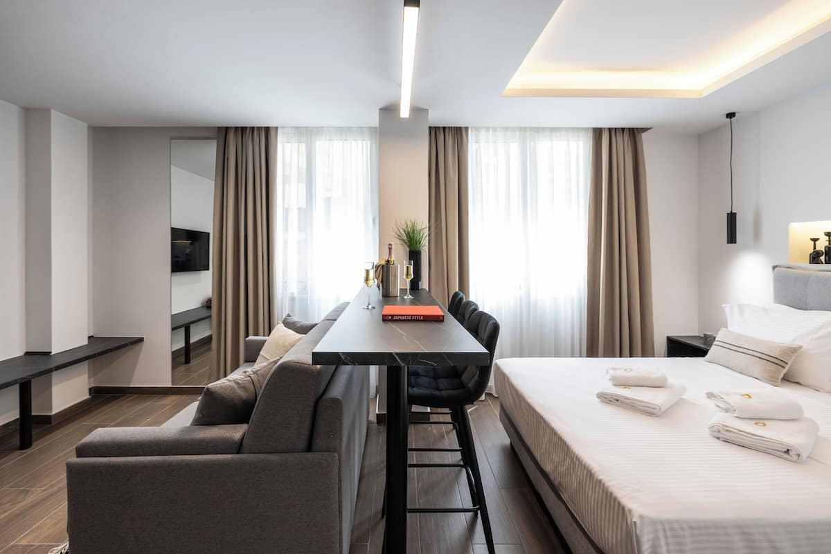 A modern hotel room with a bed, a desk, a sofa, and a dining table.