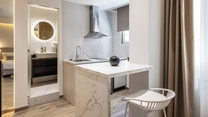 A modern kitchen with a marble island, stainless steel range hood, and a round mirror. - DOMIOS Suites Athens (Athens)