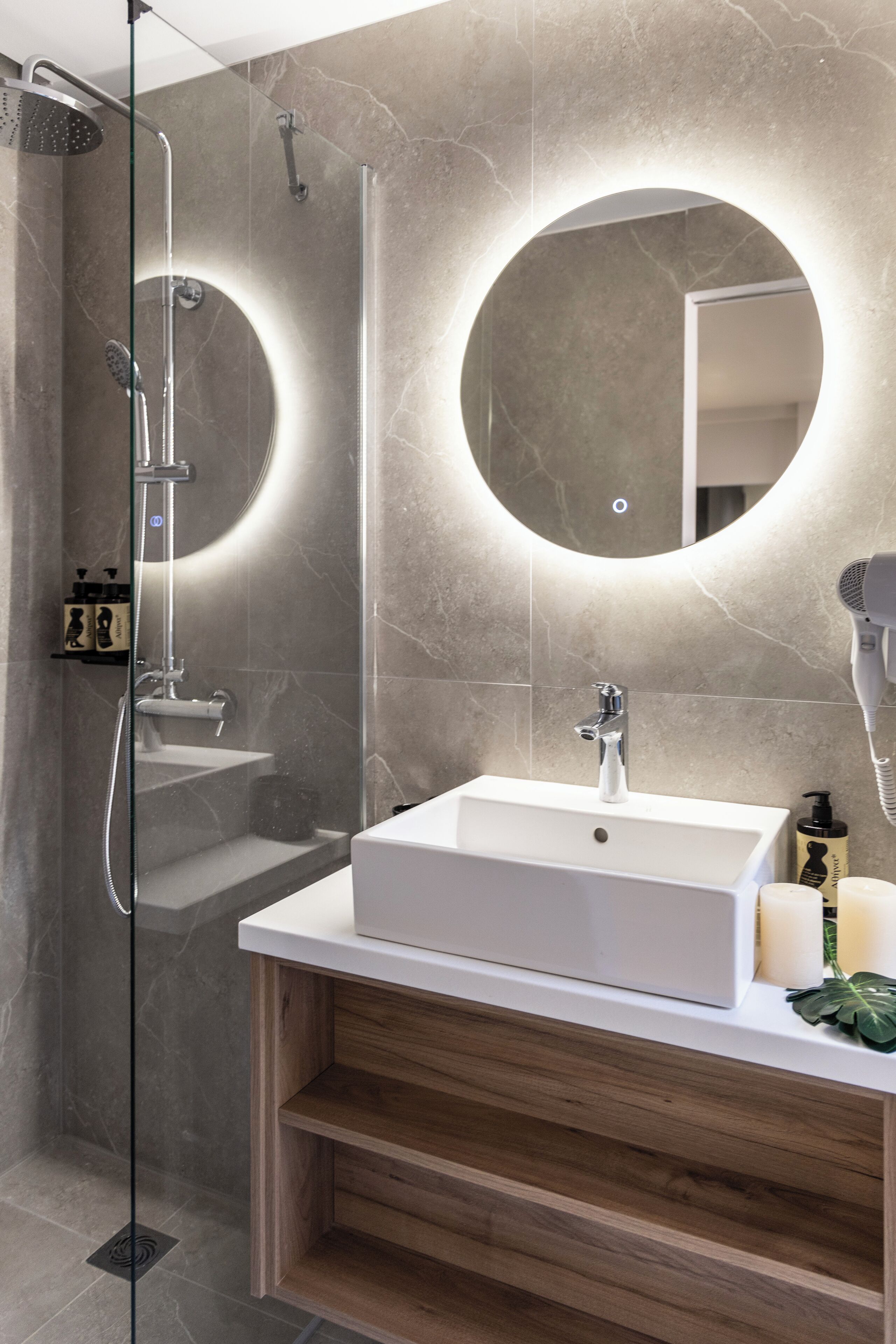 Un baño moderno con ducha de vidrio, un lavamanos blanco y un espejo redondo.