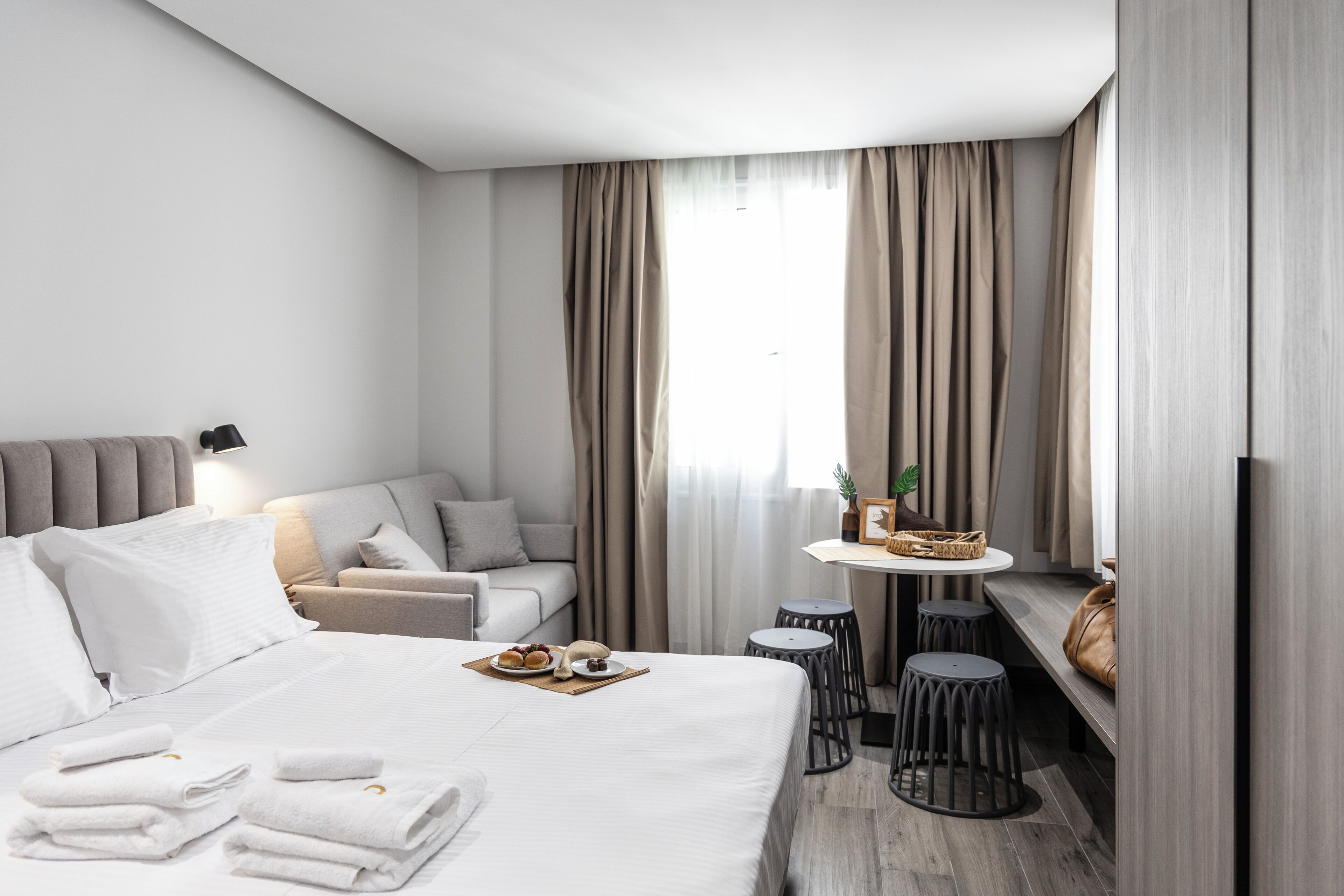 Een hotelkamer met een bed, een bank, een kleine tafel met een schaal gebakjes en een bankje.