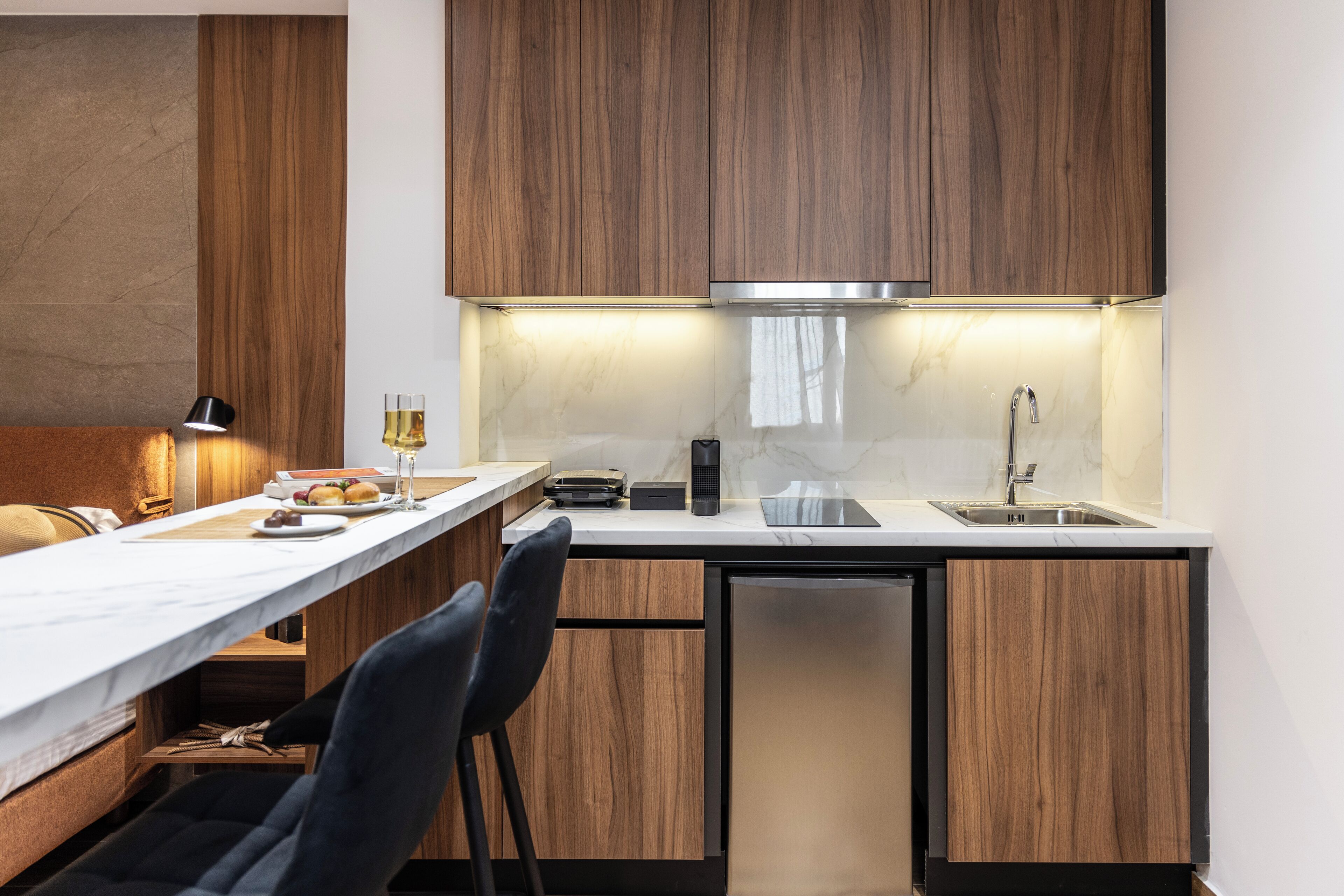 A compact kitchen with wooden cabinets, a marble countertop, and a built-in dishwasher.