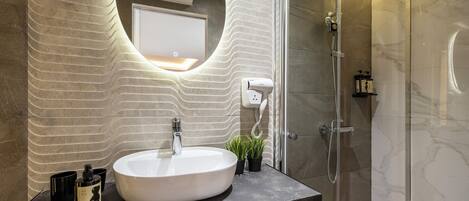 A modern bathroom with a large oval sink, a handheld showerhead, and a glass-enclosed shower.