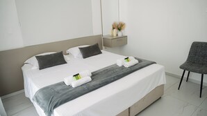 Een net opgemaakt bed met witte lakens, een grijze deken en twee handdoeken. Een grijze stoel staat naast het bed.