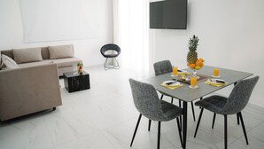 Een moderne woonkamer met een bank, eettafel en stoelen. Een flatscreen televisie hangt aan de muur.