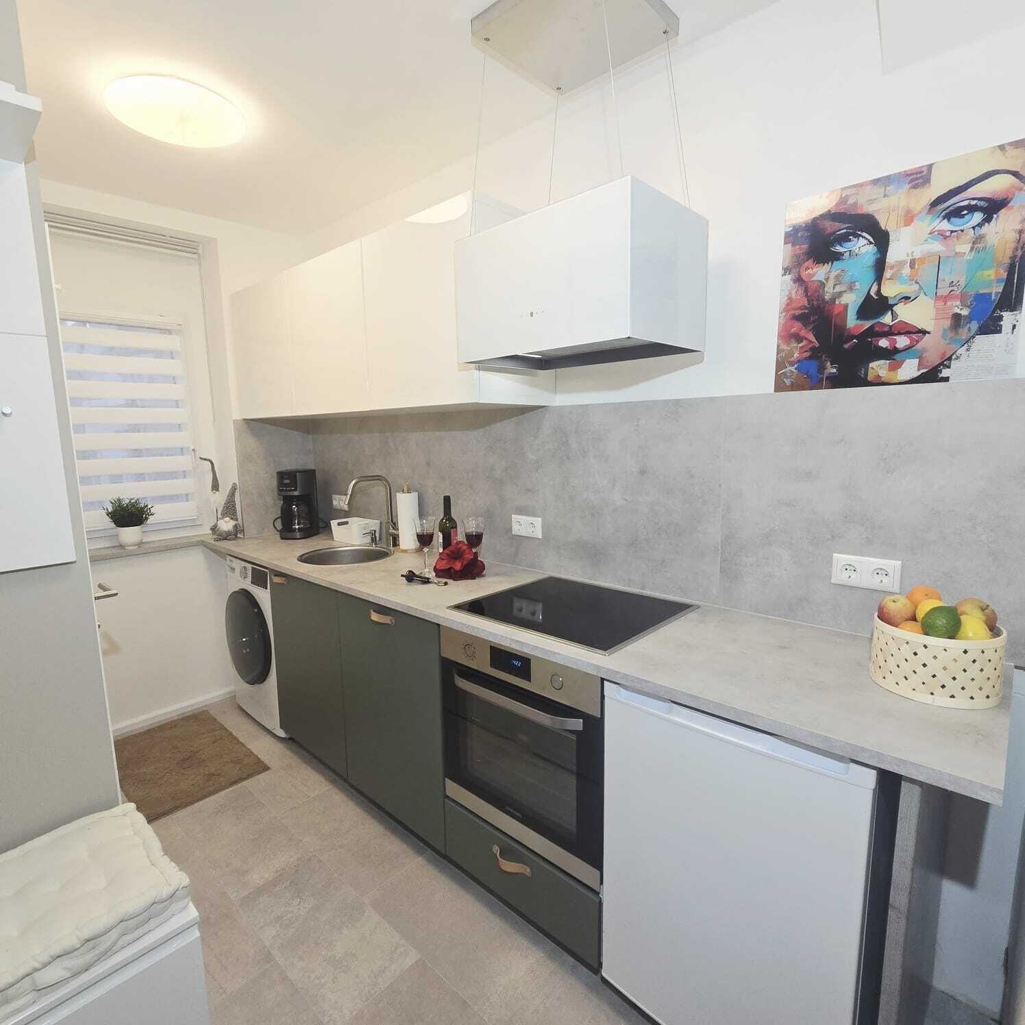 A modern kitchen with a built-in oven, a sink, and a coffee maker. There is a painting on the wall and a fruit bowl on the counter.