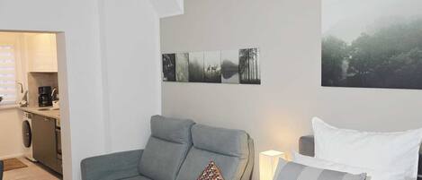 A modern bedroom with a grey sofa, a bed with white and grey bedding, and a wall-mounted artwork.