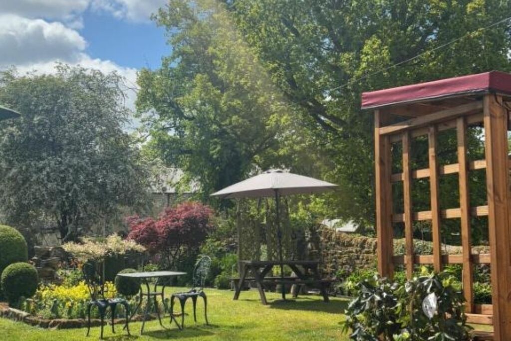 A garden with a wooden pergola, a table with chairs, and a picnic table.