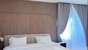 A large bed with a wooden headboard, white bedding, and a nightstand with a lamp. - Nextdoor Apartment (Kaduna)