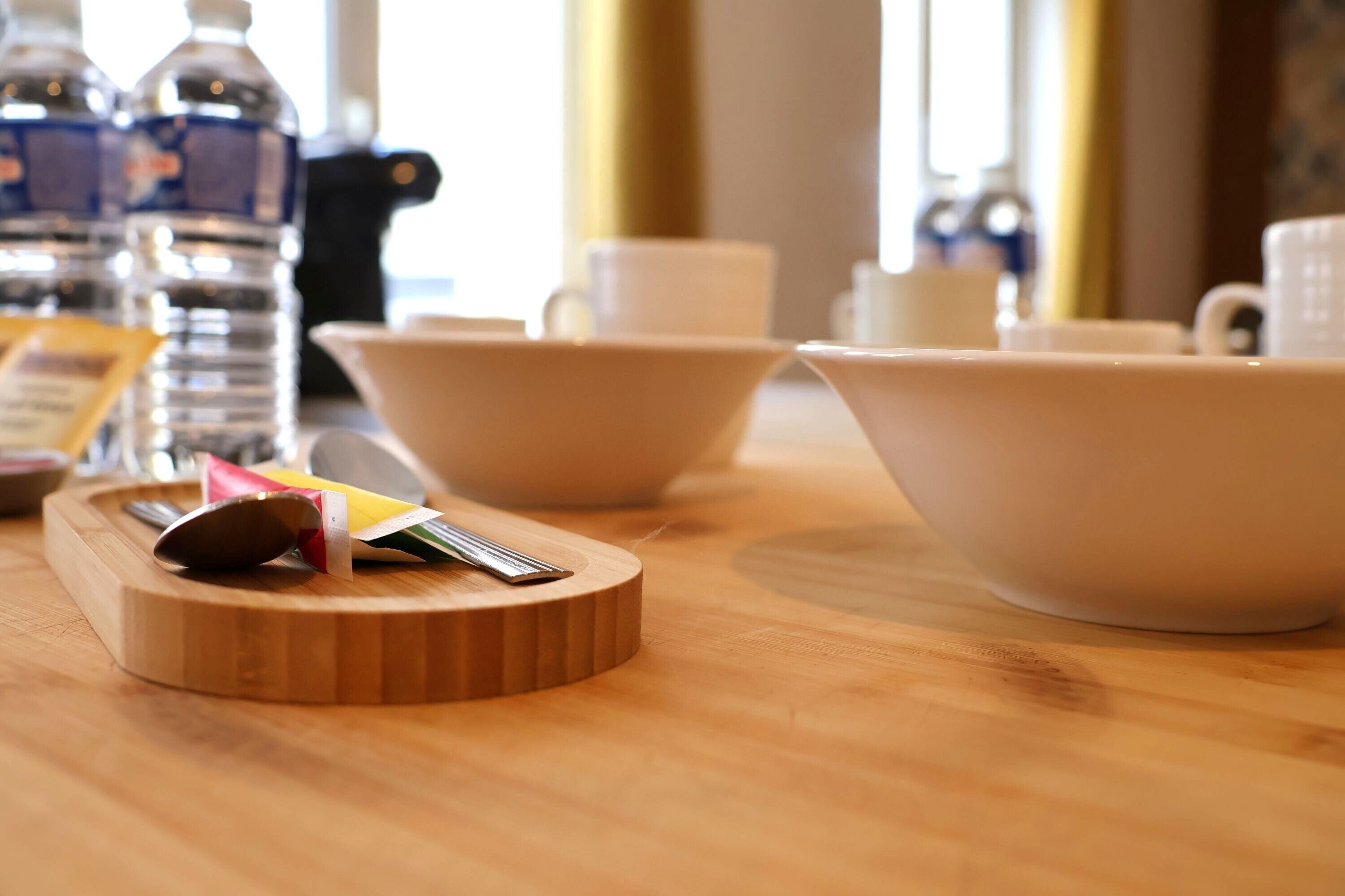 A wooden table with a cutting board, a spoon, and a packet of napkins.