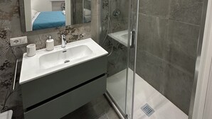 A modern bathroom with a glass-enclosed shower, a white sink with a mirror above it, and a patterned wall. - Cuore di Trastevere (Rome)