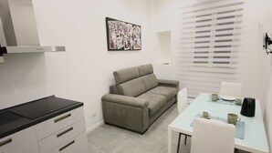 A compact living space with a kitchenette, a sofa, a dining table, and a window with blinds. - Cuore di Trastevere (Rome)