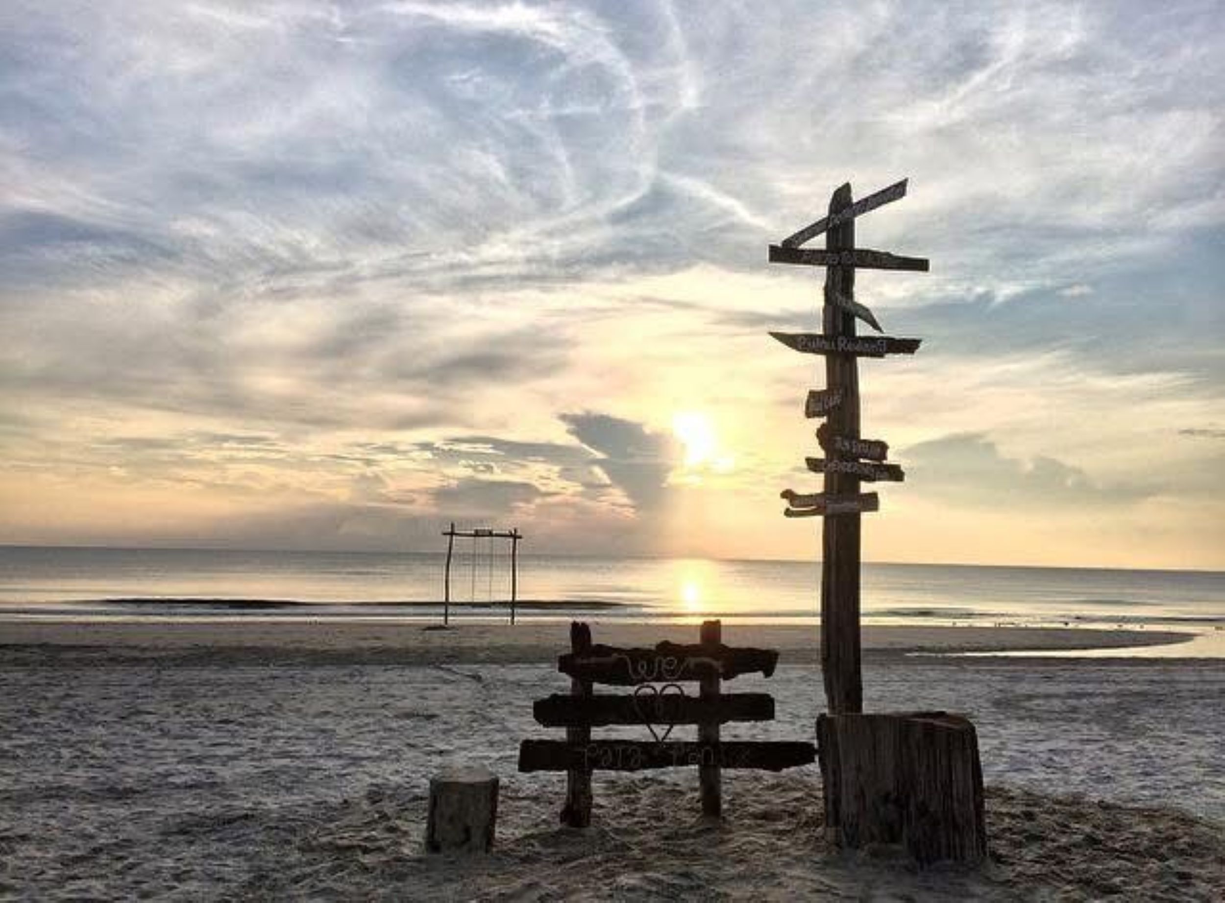 A beach with a wooden signpost and a volleyball net.