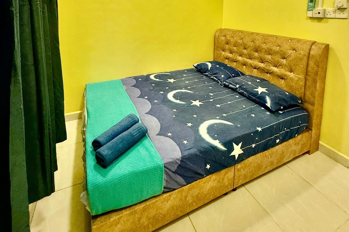 Ein kleines Zimmer mit einem Einzelbett, einer gelben Wand und einem Deckenventilator.