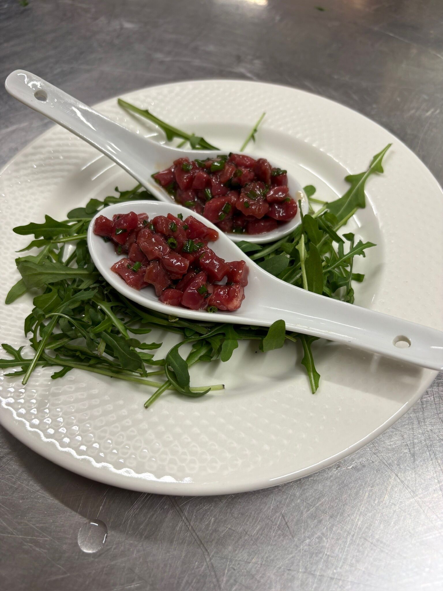 A white plate with two spoons containing a red food item, garnished with green herbs, on a textured surface.