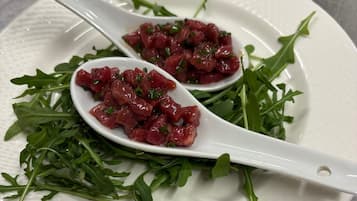 Plato blanco con dos cucharas que contienen un alimento rojo, adornado con hierbas verdes, sobre una superficie texturizada.