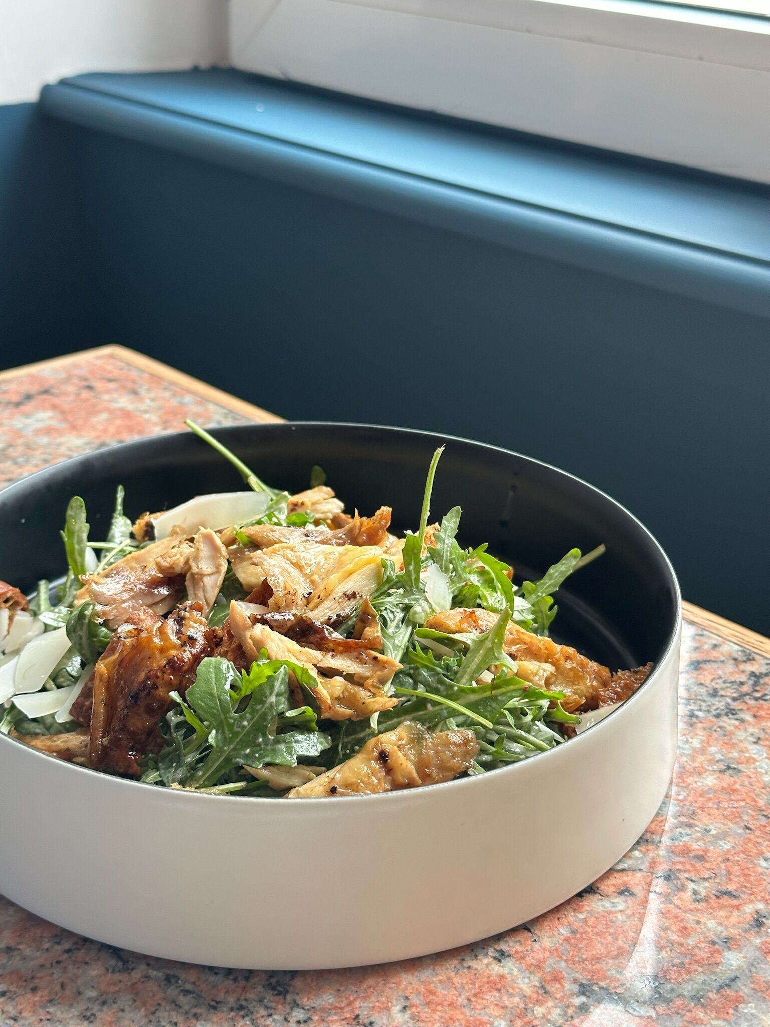 Eine Salatschüssel mit Grünzeug und Hähnchen auf einer Granitabdeckung.