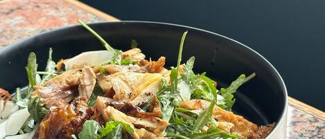 A bowl of salad with greens and chicken on a granite countertop.
