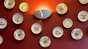 A room with a patterned sofa and a wall decorated with numerous plates. - HOTEL DE LA PAIX (Saint-Palais)