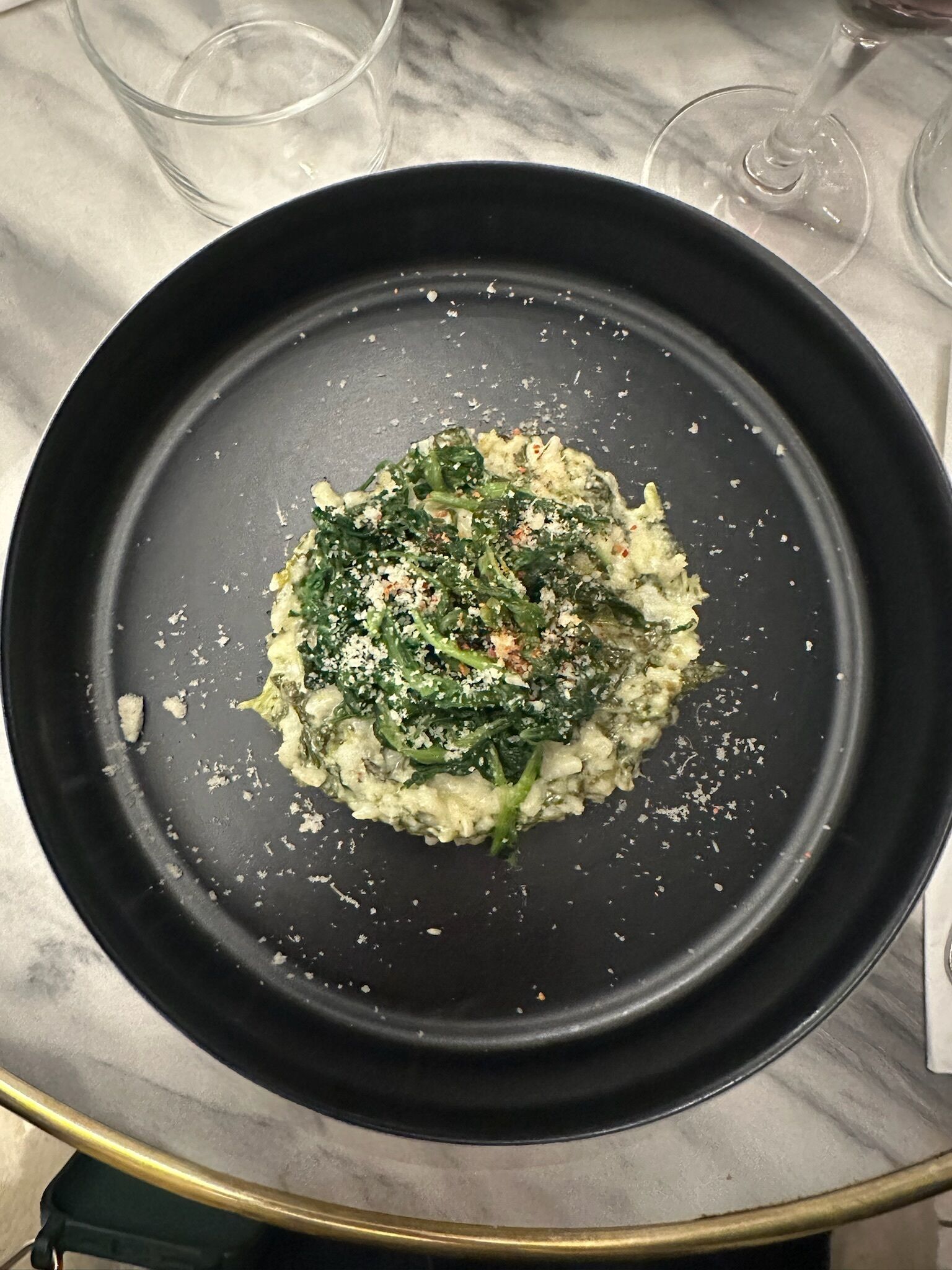 Un piatto nero con verdure e formaggio su un ripiano in marmo.