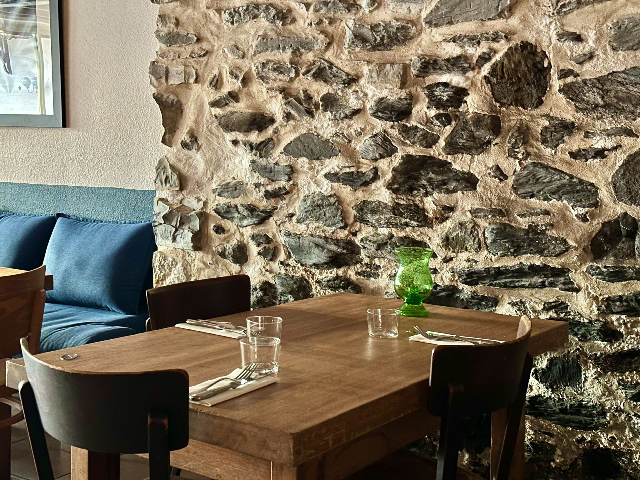 Un comedor con pared de piedra, mesa de madera, sillas y un jarrón verde.
