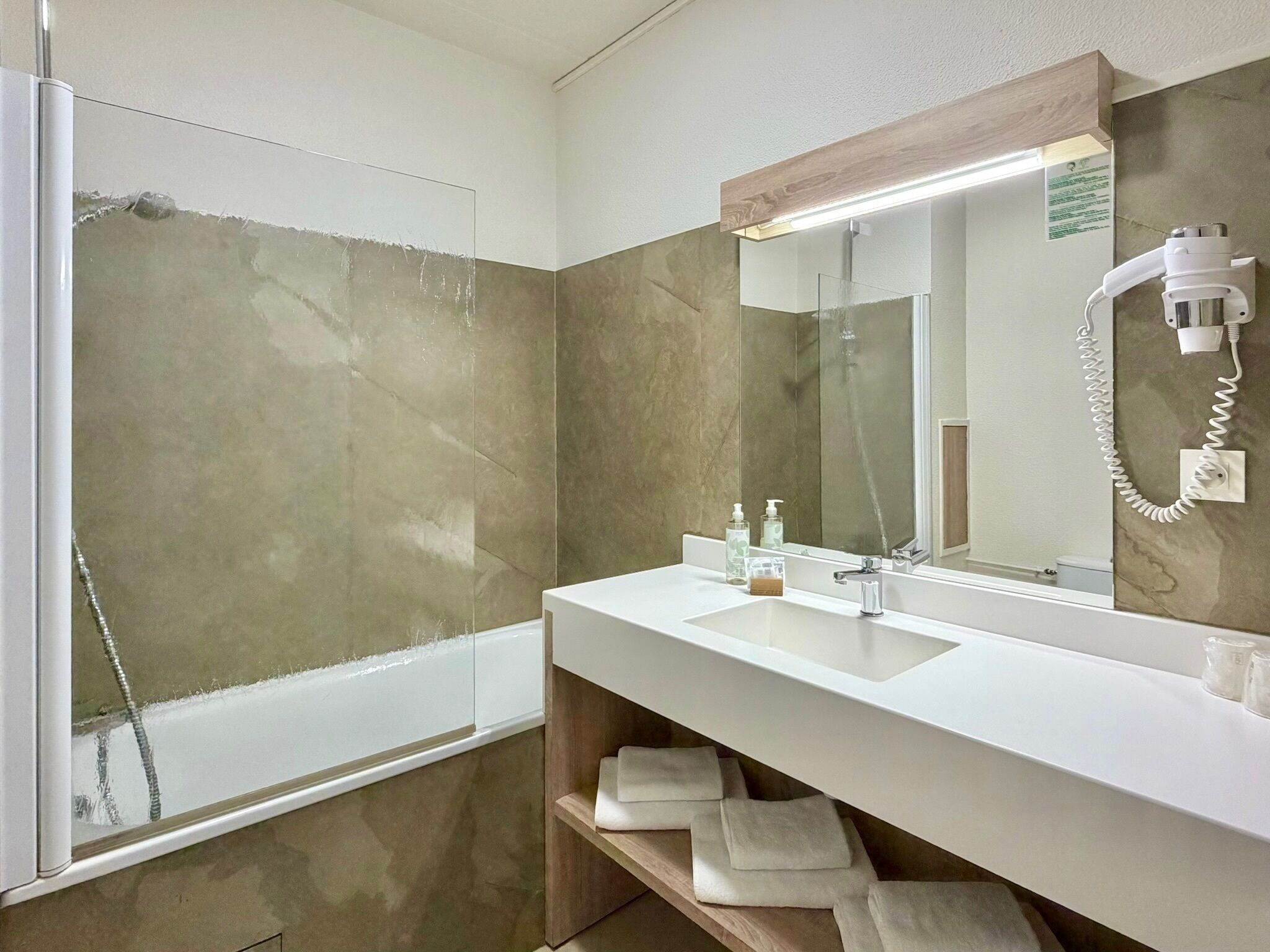 A modern bathroom with a glass shower enclosure, a white sink, a mirror, and a towel rack.