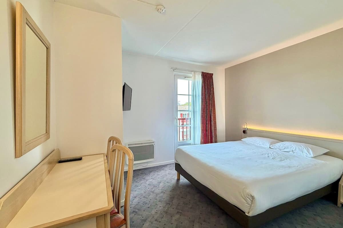 Une chambre d’hôtel avec un lit, un bureau, une chaise, une télévision et une fenêtre avec des rideaux.