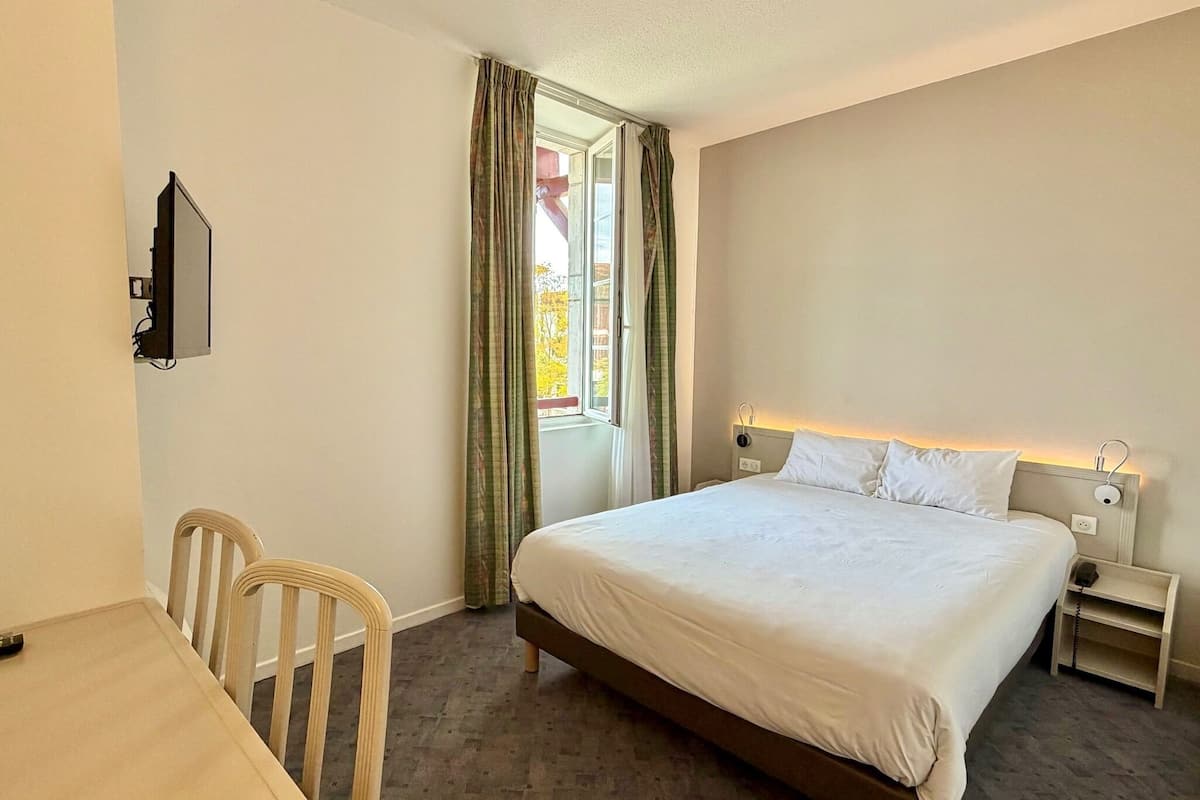 Une chambre d’hôtel équipée d’un lit, d’une table de chevet, d’une chaise et d’un téléviseur fixé au mur.