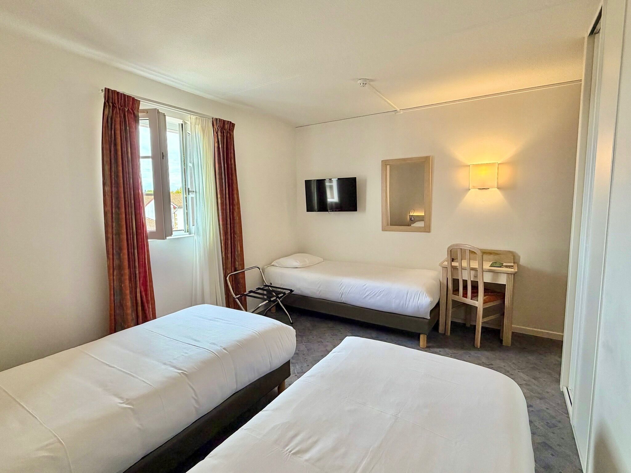 A hotel room with two single beds, a desk with a chair, a television, and a mirror.