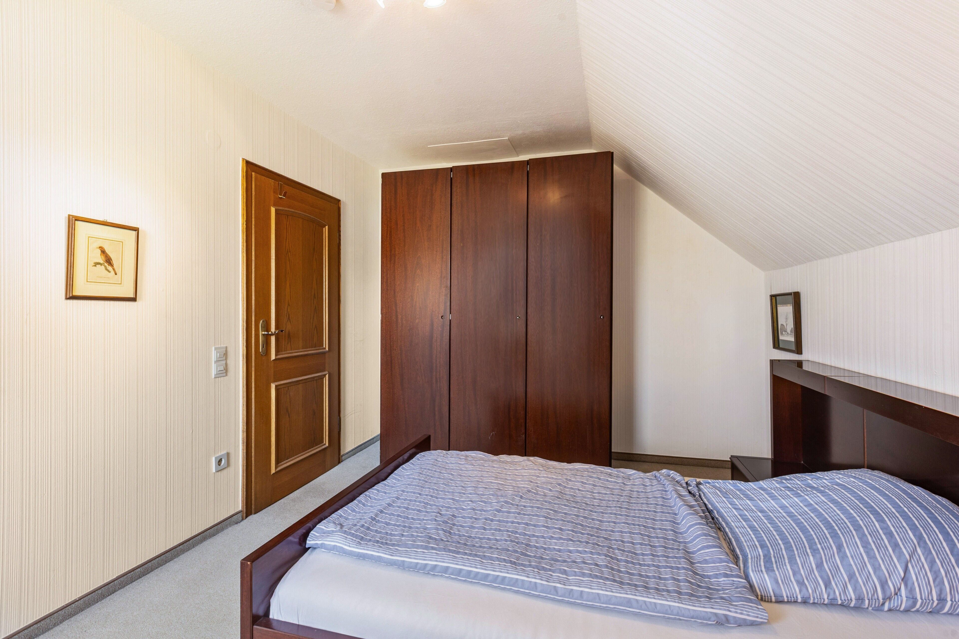 Een slaapkamer met een bed, een houten garderobe en een ingelijst schilderij aan de muur.