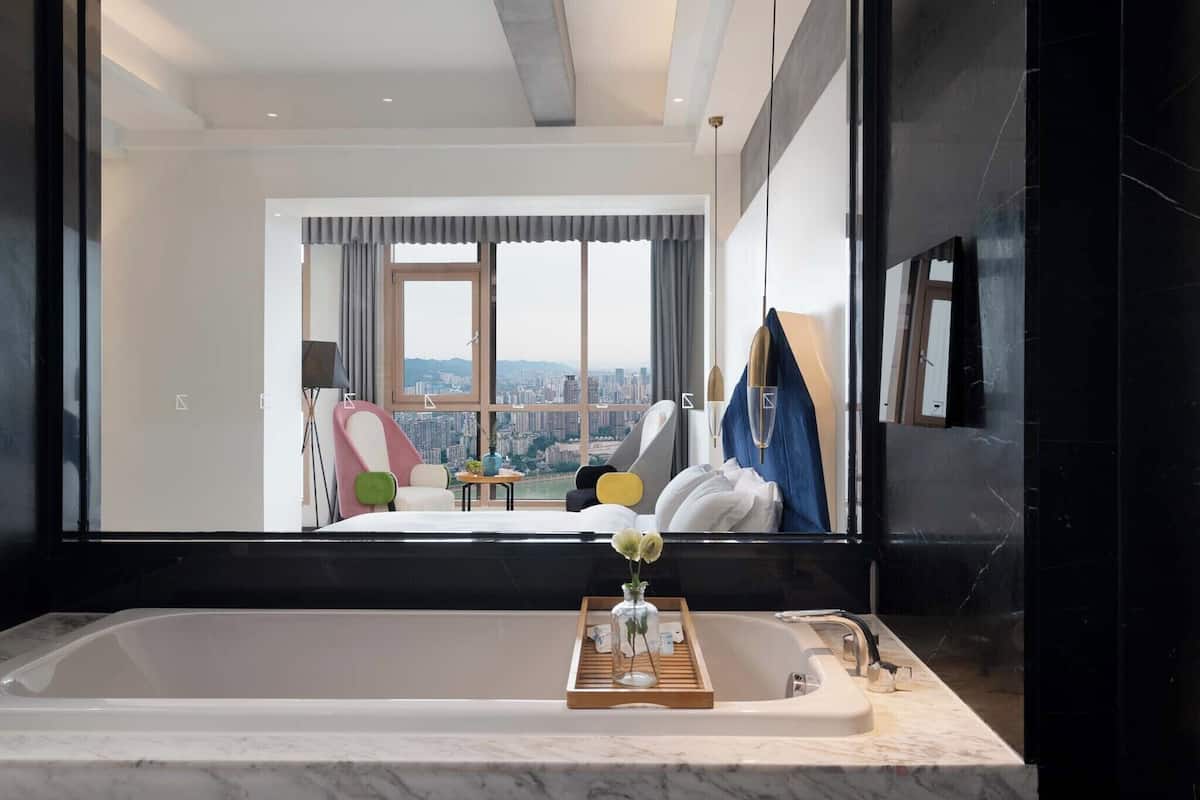 Un baño moderno con una bañera grande, una bandeja de madera con artículos de aseo y vistas a la ciudad a través de amplias ventanas.