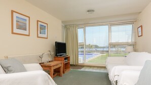 Une chambre d’hôtel avec deux lits blancs, un meuble en bois pour la télévision et une vue sur une piscine à travers de grandes fenêtres.