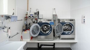 Un lavadero con dos lavadoras de carga frontal, un lavamanos y diferentes instalaciones de fontanería.