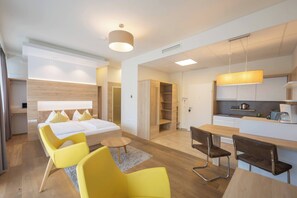 A modern hotel room with a bed, yellow chairs, a small table, a kitchen area, and a dining table. - Feelgood Studioapartment in Graz-sued 24-7 Self Check IN (Graz)