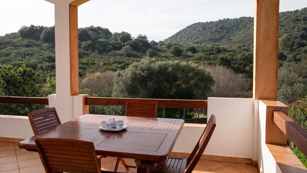 A covered outdoor dining area with a table and chairs, overlooking a hilly landscape. - Casa Leo by Wonderful Italy (Olbia)