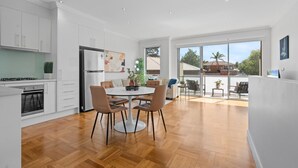 Una cocina moderna con armarios blancos, un refrigerador de acero inoxidable y un comedor con una mesa redonda y sillas.