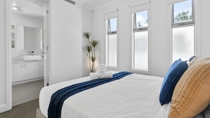 Habitación de hotel con una cama grande, un baño con espejo y lavabo, y vistas al exterior a través de las ventanas.