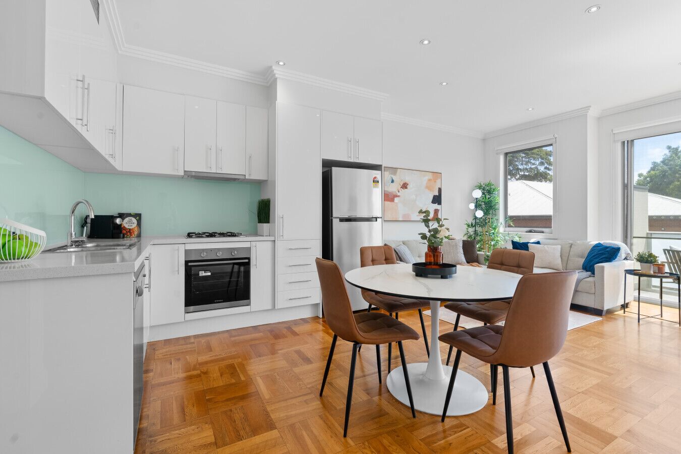 A modern kitchen with white cabinetry, a dining area with a round table and chairs, and a large window providing natural light.