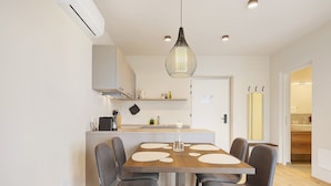 Een moderne keuken met een eethoek, met een centraal kookeiland, hanglampen en een witte inrichting.