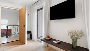 A modern room with a TV, a wooden door, a small table with a vase, and a view through a glass door. - Apartment 'Pink Lady' with Mountain View & Large Balcony (Lana)